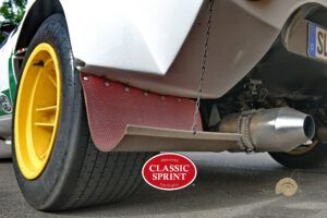 Rennwagen-Heck mit gelber Felge, rotem Schmutzfänger und Auspuff auf Asphalt.