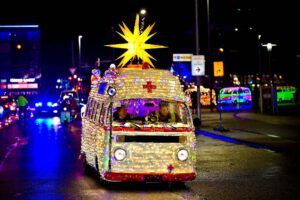 Festlich beleuchteter VW-Bus mit gelbem Stern auf dem Dach fährt nachts auf regennasser Straße.